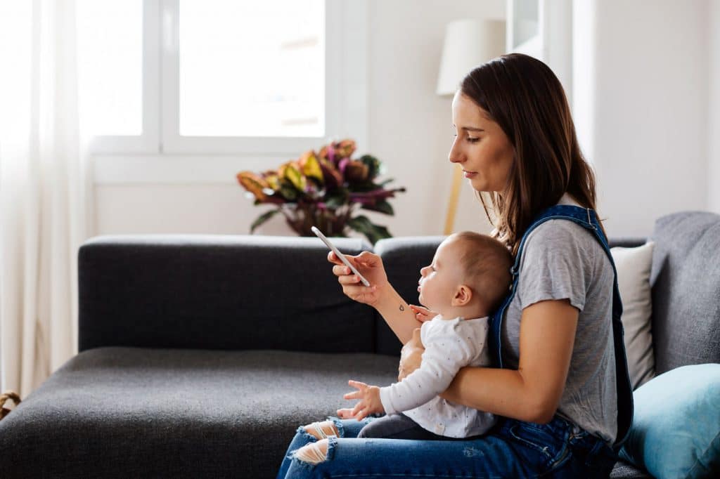 Mor med barn på fanget venter på lege, med iphone i hånden